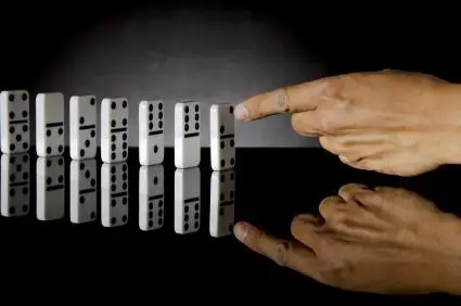 hand pushing the first domino in a line